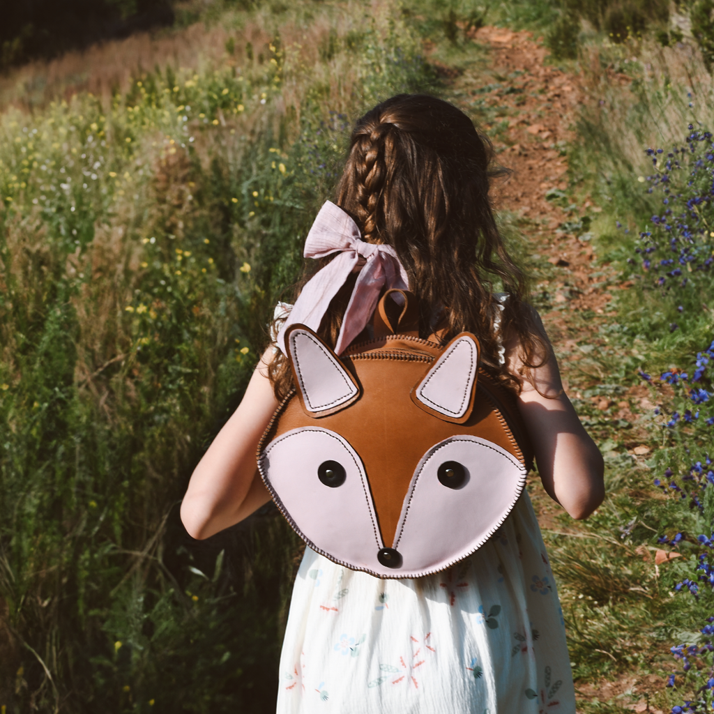 Person wearing a fox-shaped backpack with a large pink bow in a natural setting