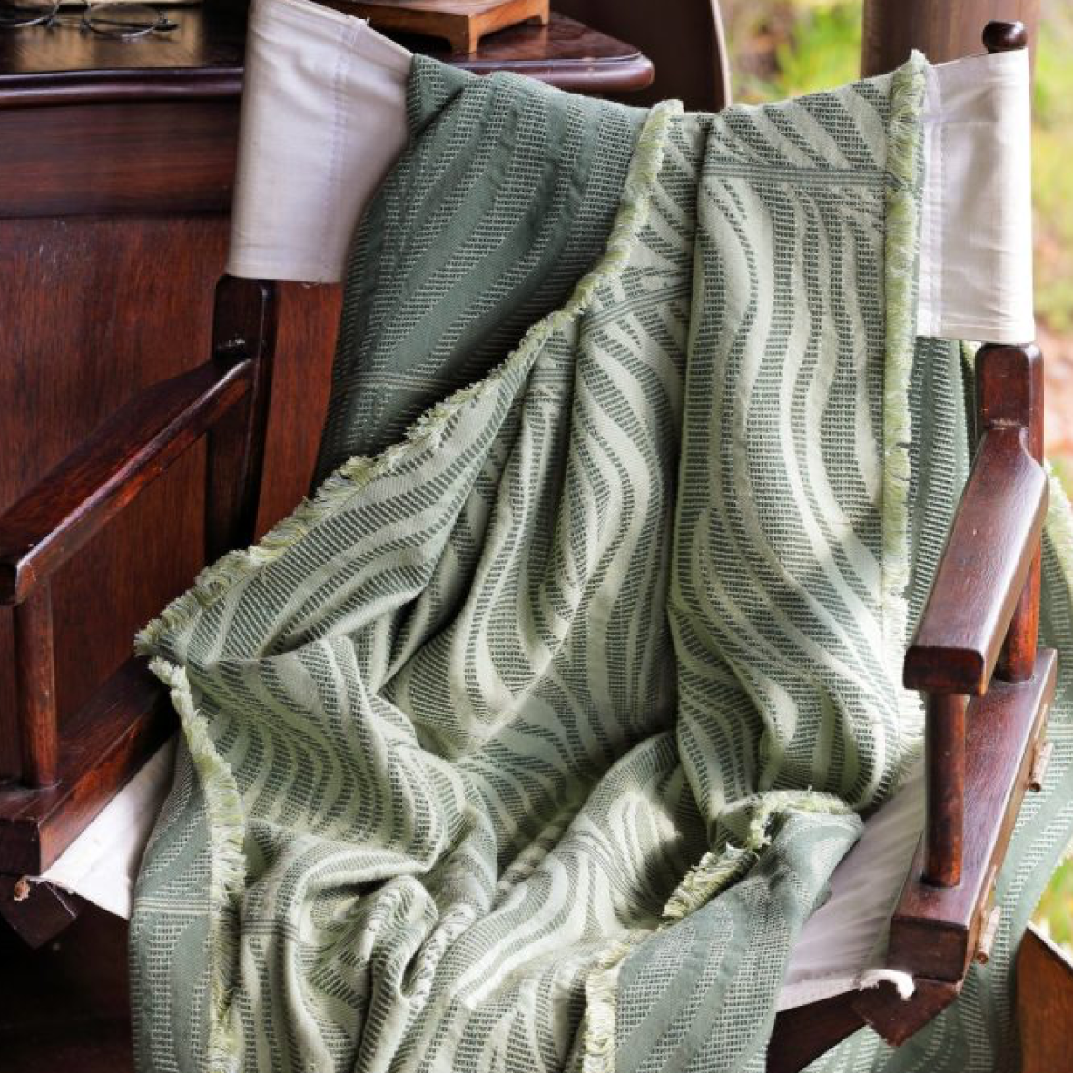Green textured blanket draped over a wooden chair with a blurred natural background