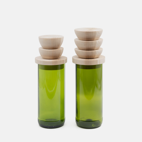 Two green glass bottles with stacked light wood lids, photographed on a clean white background.