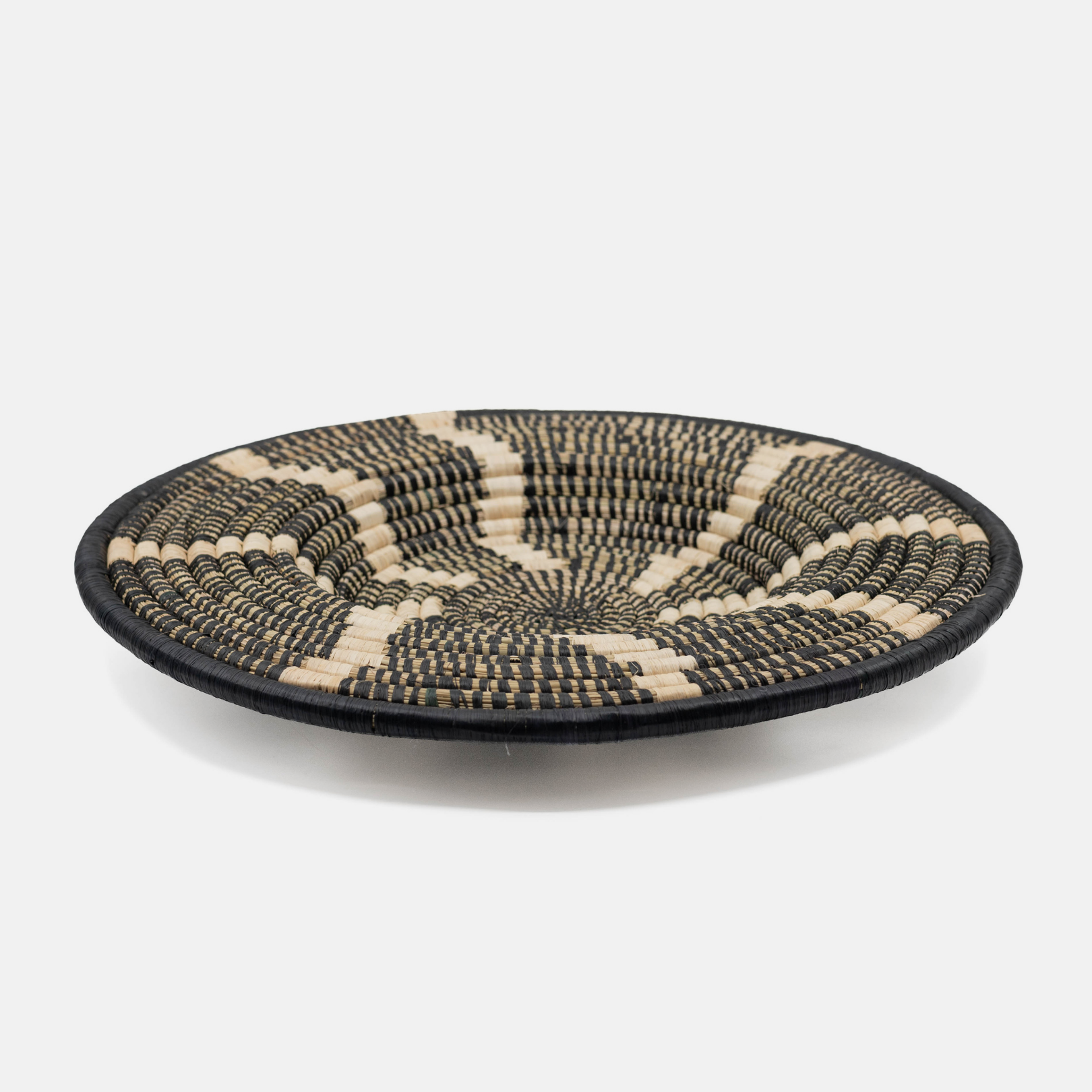 A round woven basket tray with a black and natural beige geometric pattern, photographed on a clean white background.