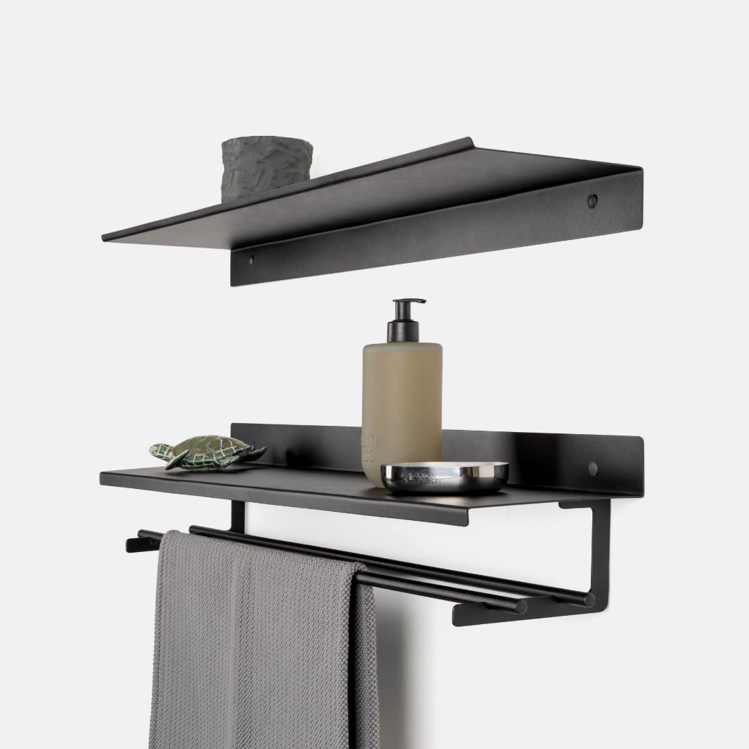 Black metal wall-mounted bathroom shelf set with a towel bar, shown with a gray towel, soap dispenser, small bowl, and decorative item against a light gray background.