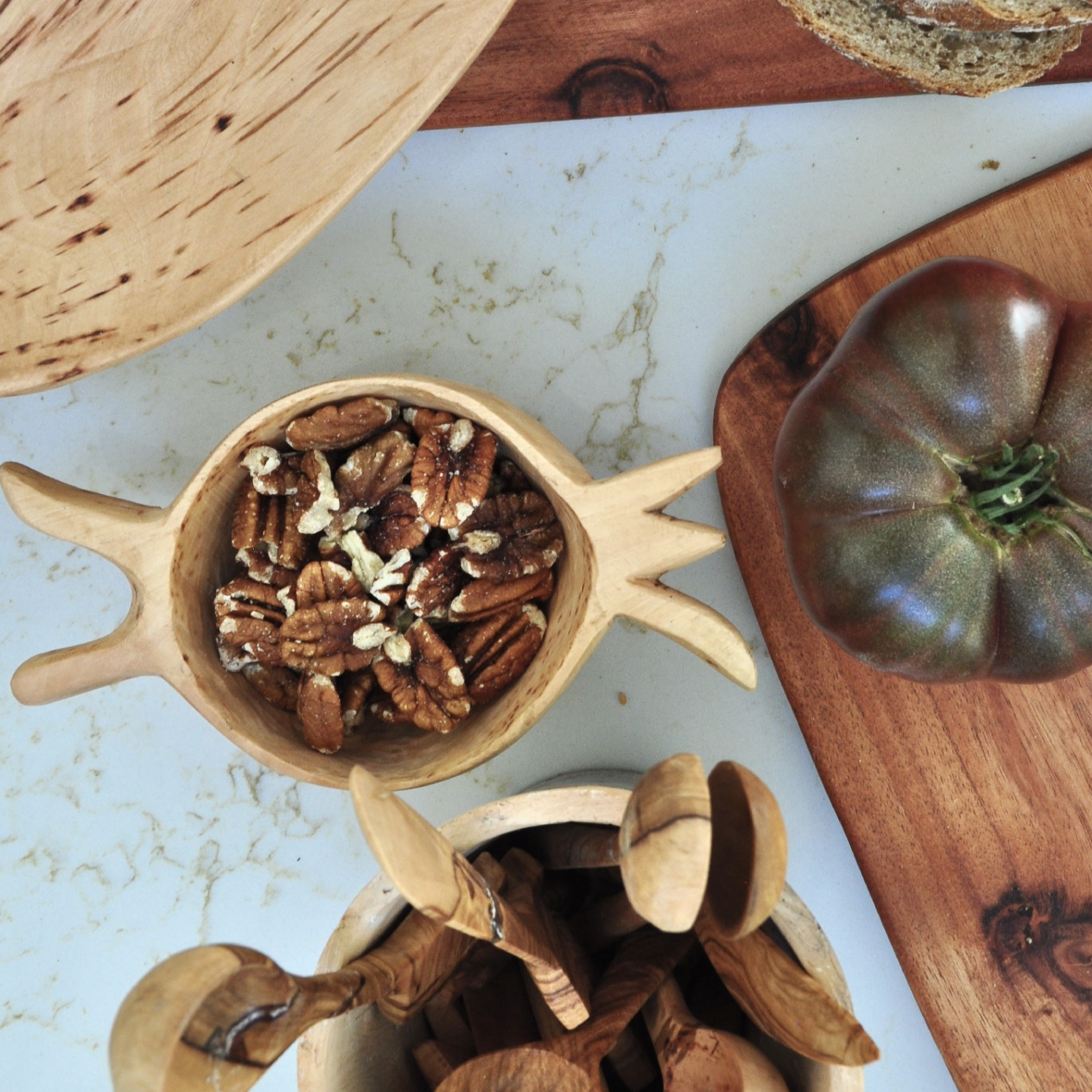 Wooden bowl with pecans on a marble surface with a tomato and bread.