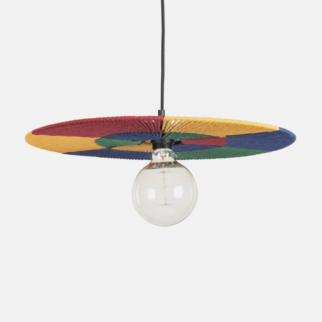 A modern pendant light with a wide, circular woven shade in red, yellow, green, and blue, suspending a clear glass globe bulb against a light gray background.