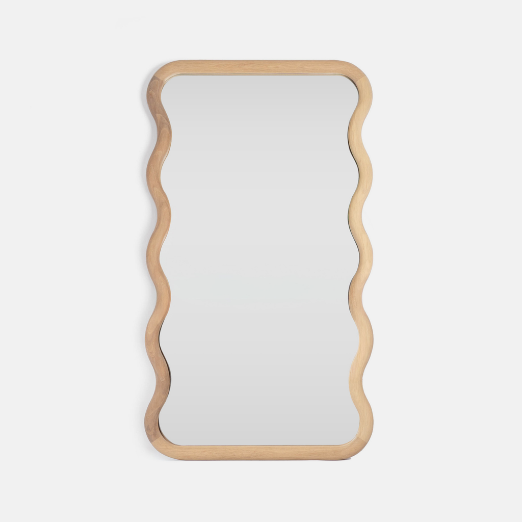 A solid oak vanity mirror with a wavy edge design on a light grey background