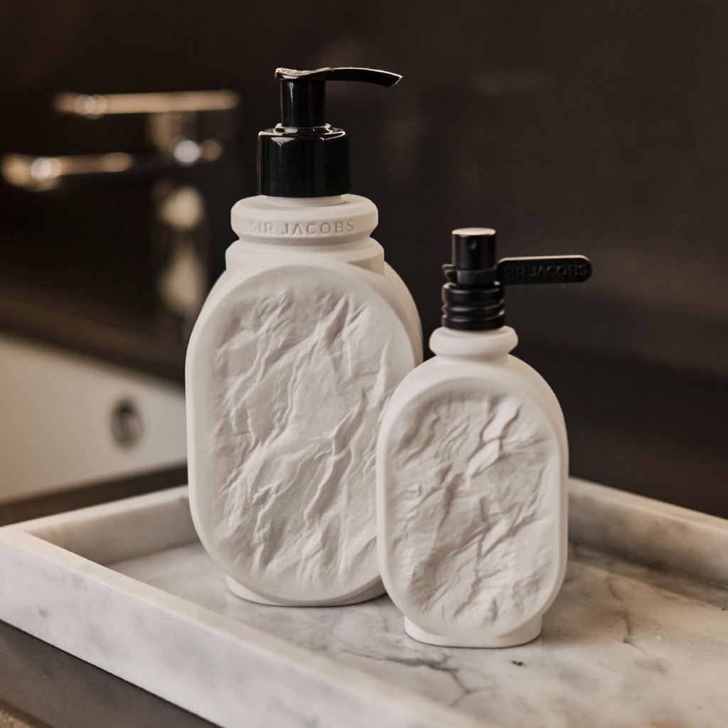 Two white ceramic bottles with black pumps on a marble surface.